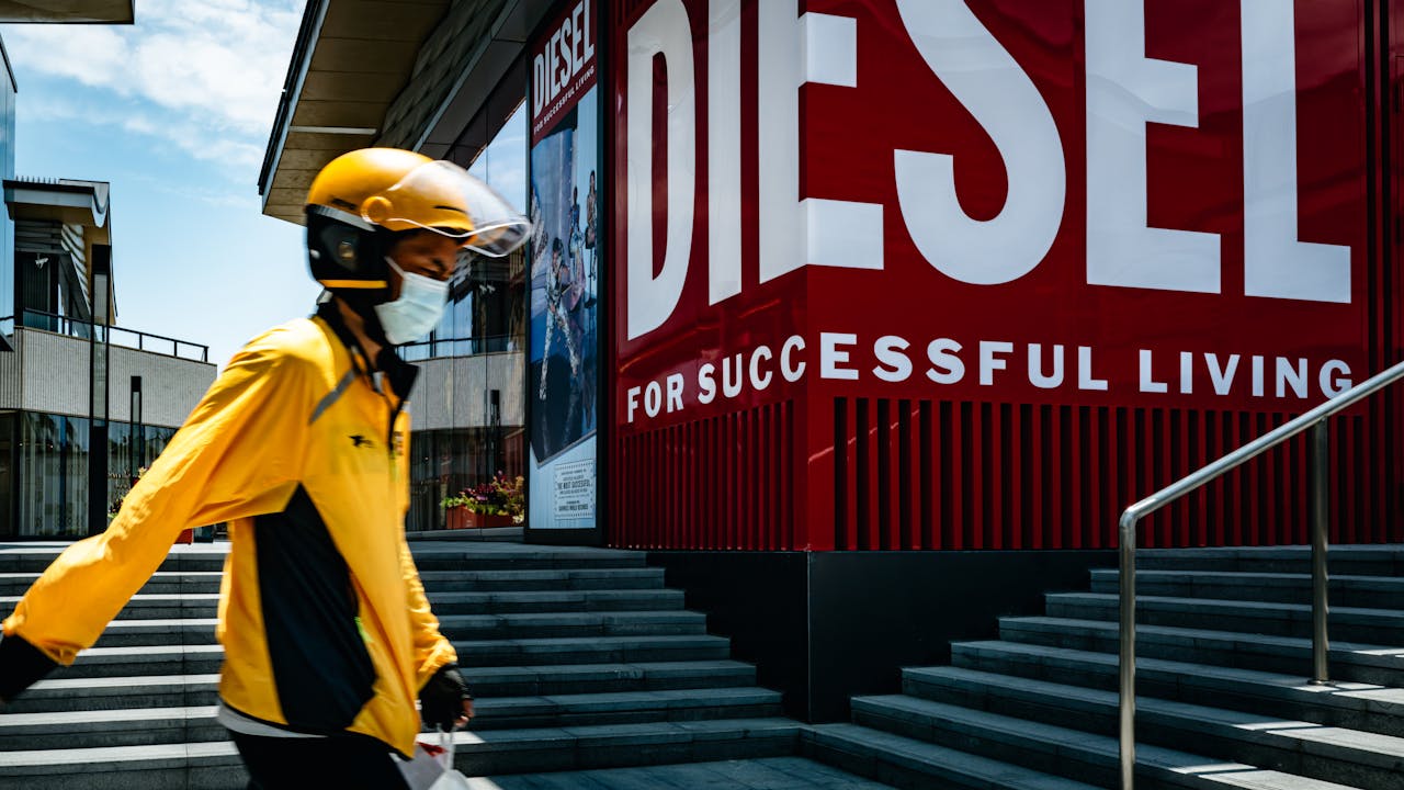 Delivery courier in yellow uniform passing Diesel storefront in sunny Suzhou, China.